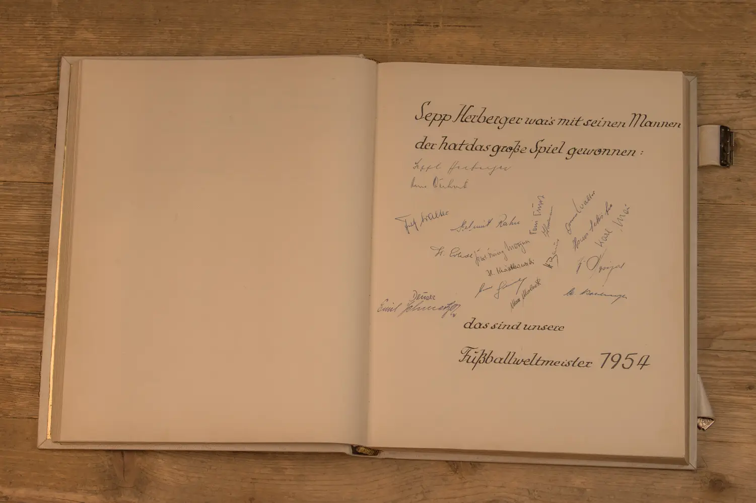 Geöffnetes Buch zeigt handgeschriebenen Text mit dem Titel "Sepp Herberger war’s mit seinen Mannen, der hat das große Spiel gewonnen," gefolgt von mehreren Unterschriften und dem Hinweis "das sind unsere Fußballweltmeister 1954.