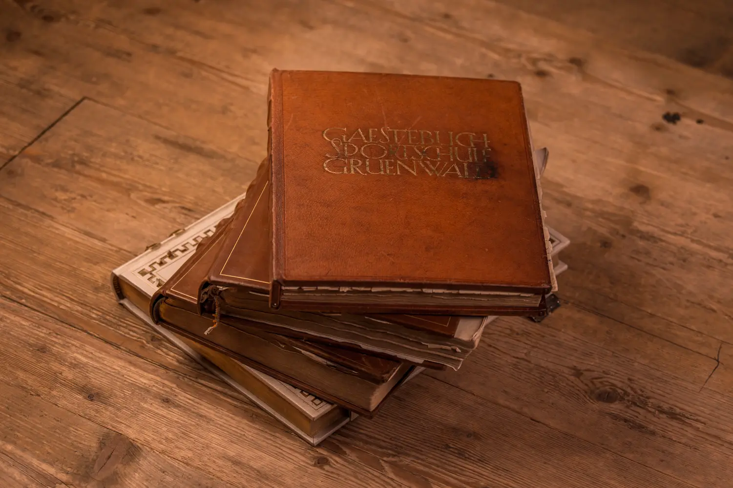 Stapel alter, gebundener Bücher auf einem Holzboden, das oberste Buch trägt den Titel "Gästebuch Sportschule Grünwald".