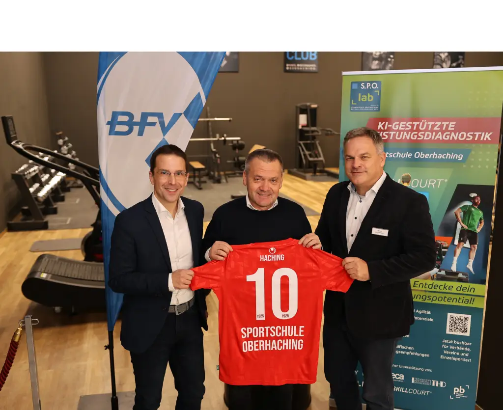 Auf dem Foto stehen drei Männer in einem Trainings- und Diagnostikbereich der Sportschule Oberhaching. Links ist BFV-Präsident Dr. Christoph Kern, in der Mitte SpVgg Unterhaching-Präsident Manfred Schwabl und rechts SPO-Geschäftsführer Markus Mayer zu sehen. Gemeinsam halten sie ein rotes Trikot mit der Aufschrift „Haching“ sowie „Sportschule Oberhaching“ und der Rückennummer 10 in die Kamera. Im Hintergrund sind Trainingsgeräte, eine BFV-Fahne sowie ein S.P.O. lab-Roll-up mit dem Thema „KI-gestützte Leistungsdiagnostik“ erkennbar.