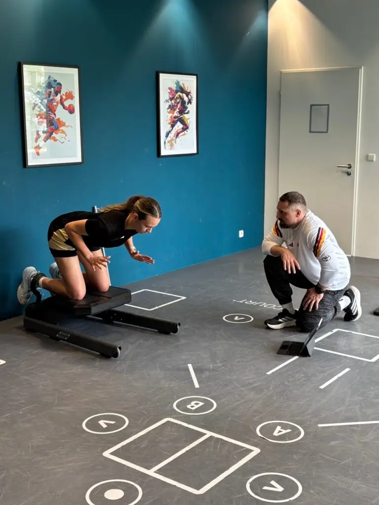Basketballspielerin absolviert an der Sportschule Oberhaching einen leistungsdiagnostischen Test auf einer Trainingsplattform, w&auml;hrend ein Athletiktrainer die Bewegung beobachtet und die Messung begleitet.