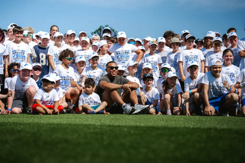 Große Gruppe von Kindern und Jugendlichen beim gemeinsamen Gruppenfoto eines American-Football-Camps auf einem Kunstrasenplatz.“