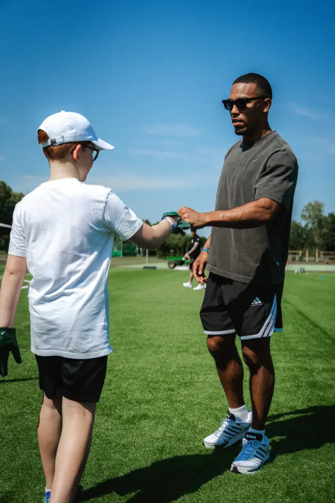 Kind und Trainer begrüßen sich mit einem Fist Bump auf einem Kunstrasenplatz während eines Football-Camps.