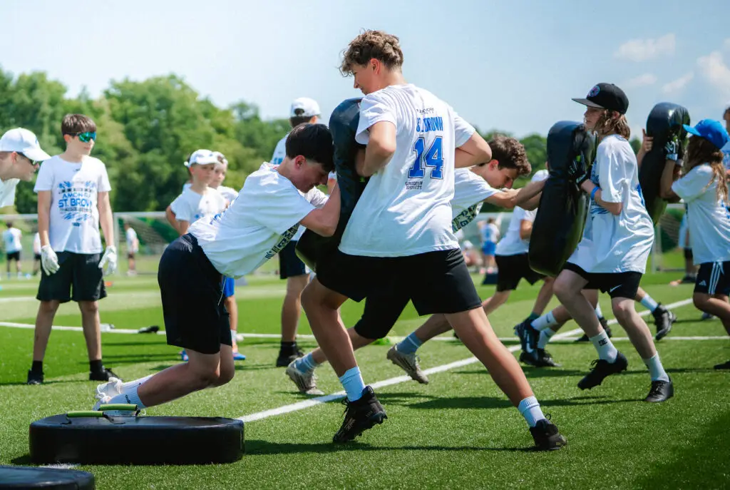 Kinder und Jugendliche trainieren Tackling- und Blocktechniken mit Prallschilden während einer Übungseinheit auf dem Football-Feld.
