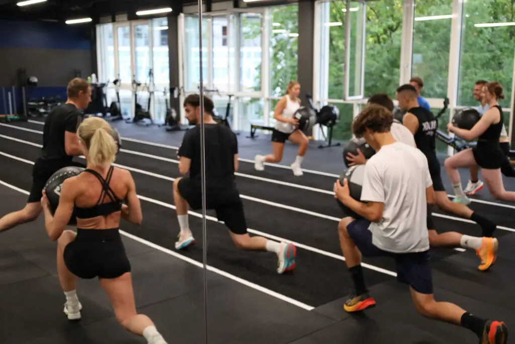 Gruppe absolviert Ausfallschritte mit Wallballs beim HYROX-Training im S.P.O. Club der Sportschule Oberhaching.