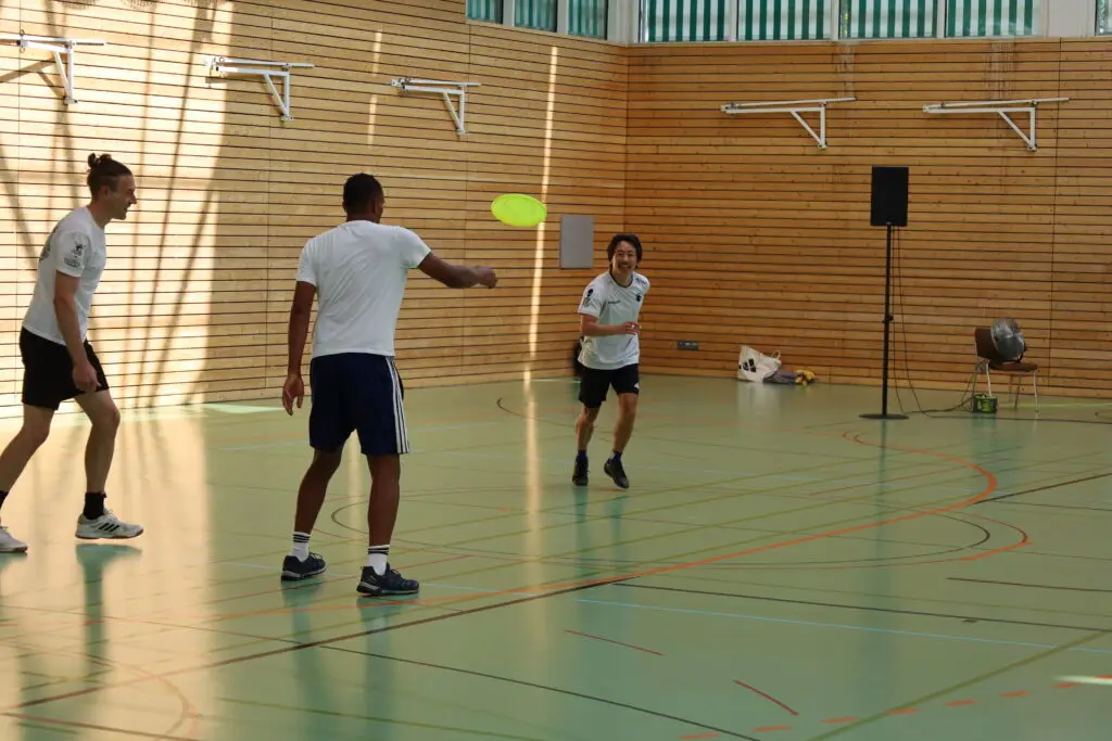 Bildergalerie vom Frisbee Festival M&uuml;nchen an der Sportschule Oberhaching mit Spielszenen auf dem Sportplatz und in der Halle, Turnierst&auml;nden, Zuschauerinnen und Zuschauern sowie verschiedenen Frisbee-Disziplinen wie Disc Golf, Ultimate Frisbee und Freestyle.