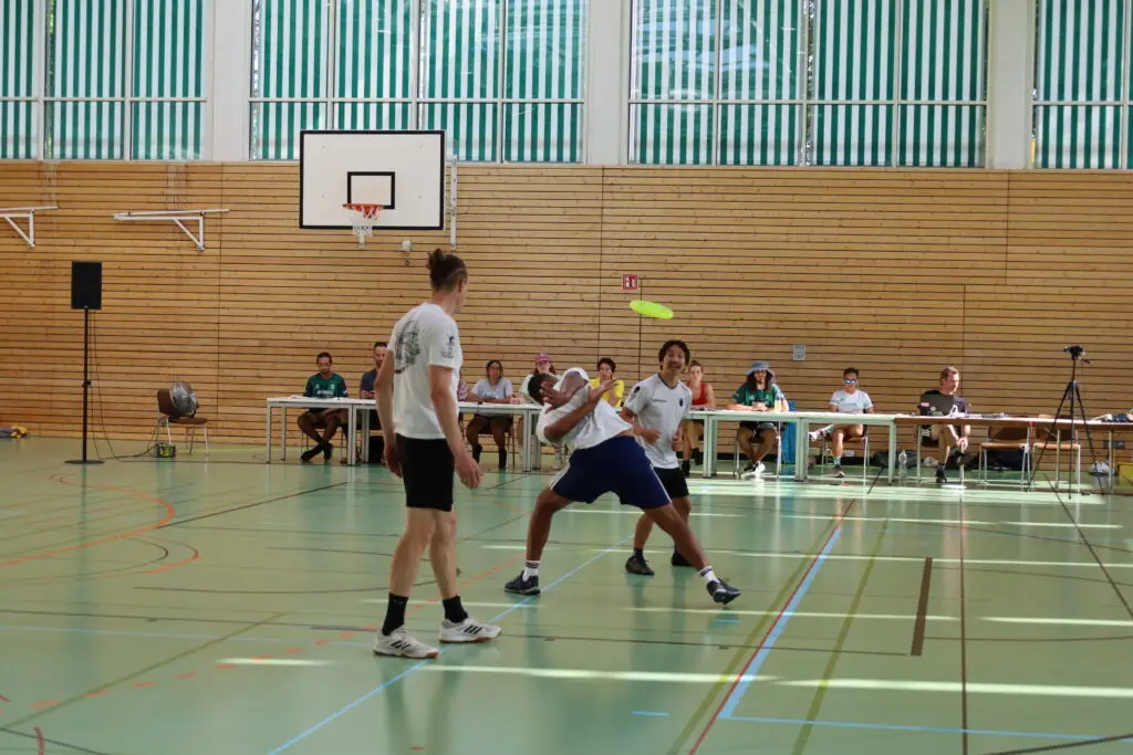 Bildergalerie vom Frisbee Festival M&uuml;nchen an der Sportschule Oberhaching mit Spielszenen auf dem Sportplatz und in der Halle, Turnierst&auml;nden, Zuschauerinnen und Zuschauern sowie verschiedenen Frisbee-Disziplinen wie Disc Golf, Ultimate Frisbee und Freestyle.