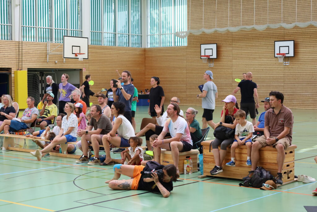 Bildergalerie vom Frisbee Festival M&uuml;nchen an der Sportschule Oberhaching mit Spielszenen auf dem Sportplatz und in der Halle, Turnierst&auml;nden, Zuschauerinnen und Zuschauern sowie verschiedenen Frisbee-Disziplinen wie Disc Golf, Ultimate Frisbee und Freestyle.