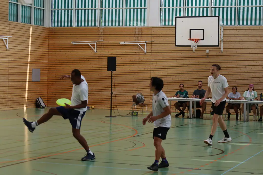 Bildergalerie vom Frisbee Festival M&uuml;nchen an der Sportschule Oberhaching mit Spielszenen auf dem Sportplatz und in der Halle, Turnierst&auml;nden, Zuschauerinnen und Zuschauern sowie verschiedenen Frisbee-Disziplinen wie Disc Golf, Ultimate Frisbee und Freestyle.