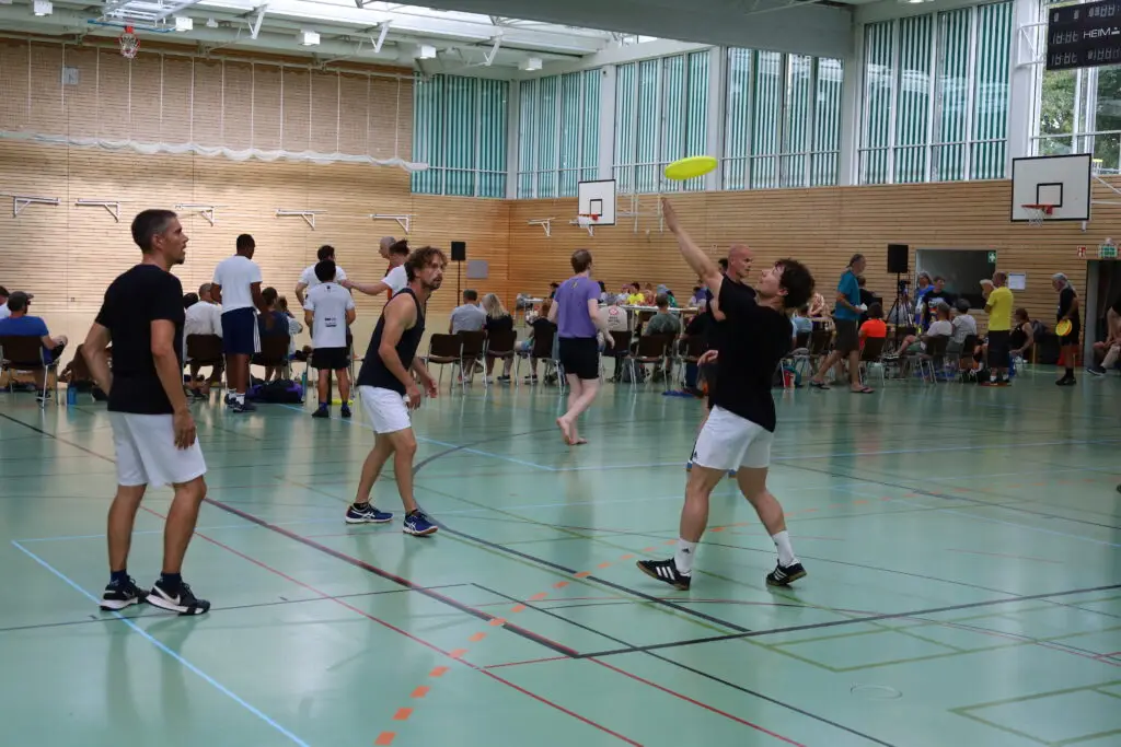 Bildergalerie vom Frisbee Festival M&uuml;nchen an der Sportschule Oberhaching mit Spielszenen auf dem Sportplatz und in der Halle, Turnierst&auml;nden, Zuschauerinnen und Zuschauern sowie verschiedenen Frisbee-Disziplinen wie Disc Golf, Ultimate Frisbee und Freestyle.