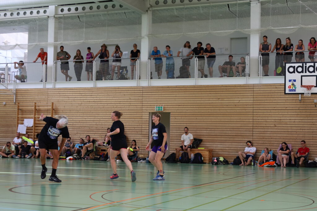 Bildergalerie vom Frisbee Festival M&uuml;nchen an der Sportschule Oberhaching mit Spielszenen auf dem Sportplatz und in der Halle, Turnierst&auml;nden, Zuschauerinnen und Zuschauern sowie verschiedenen Frisbee-Disziplinen wie Disc Golf, Ultimate Frisbee und Freestyle.