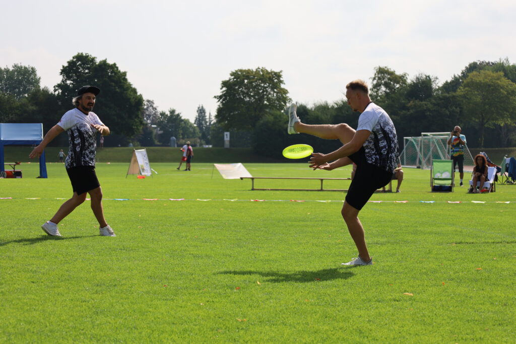 Bildergalerie vom Frisbee Festival M&uuml;nchen an der Sportschule Oberhaching mit Spielszenen auf dem Sportplatz und in der Halle, Turnierst&auml;nden, Zuschauerinnen und Zuschauern sowie verschiedenen Frisbee-Disziplinen wie Disc Golf, Ultimate Frisbee und Freestyle.