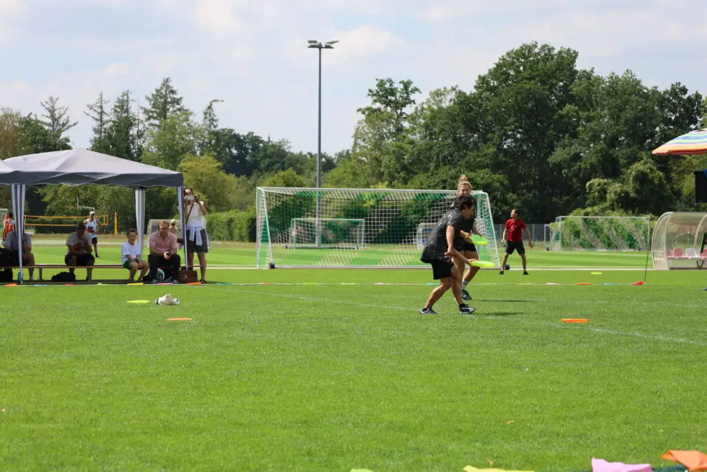 Bildergalerie vom Frisbee Festival M&uuml;nchen an der Sportschule Oberhaching mit Spielszenen auf dem Sportplatz und in der Halle, Turnierst&auml;nden, Zuschauerinnen und Zuschauern sowie verschiedenen Frisbee-Disziplinen wie Disc Golf, Ultimate Frisbee und Freestyle.